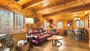A cozy log cabin interior with a fireplace, leather sofa, wooden dining table, and rustic decor.