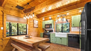 A wooden cabin kitchen with a wooden table, benches, a stove, microwave, and green cabinets.