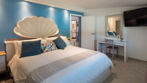 A bedroom with a large bed, a desk, a chair, a TV, and a bathroom visible through an open door.