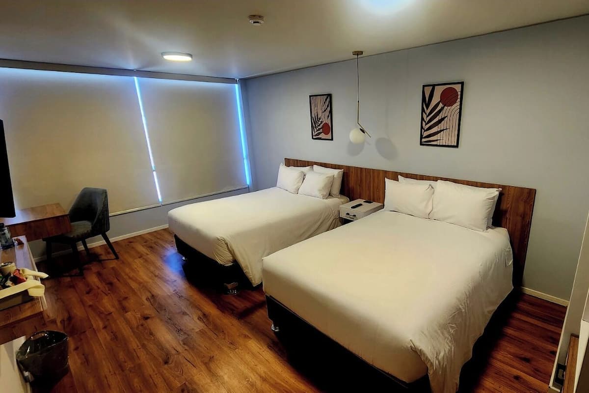 Habitación de hotel con dos camas, un escritorio, una silla y obras de arte en las paredes.