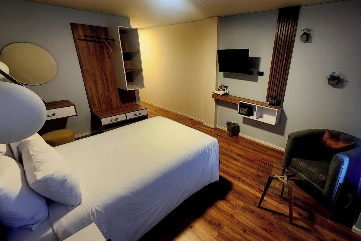 Habitación de hotel con cama, una silla, televisor y piso de madera.