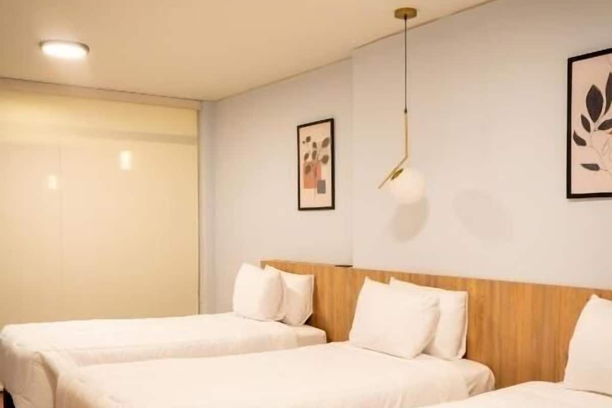 Habitación de hotel con dos camas, cabeceros de madera, ropa de cama blanca y una lámpara en el techo.
