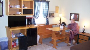 A compact room with a wooden desk, a television, a radiator, a bench, and a small cabinet. - Cozy Campground Cabin Cottage with WiFi and AC in charming Greybull (Greybull)