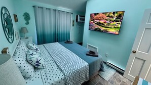 Makuuhuone, jossa on sänky, verhot, televisio ja seinälle ripustettu taulu.