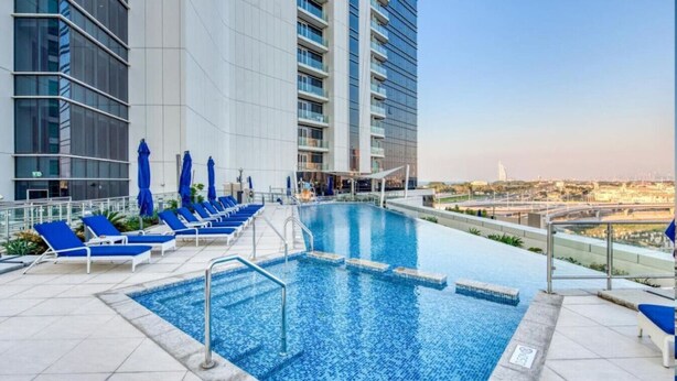 Una piscina sul tetto con piastrelle blu, circondata da lettini e ombrelloni, con vista sulla città.