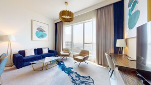 Una camera d'albergo moderna con un divano blu, un tavolino da caffè, due poltrone, una scrivania con una lampada e un'ampia finestra con vista sulla città.