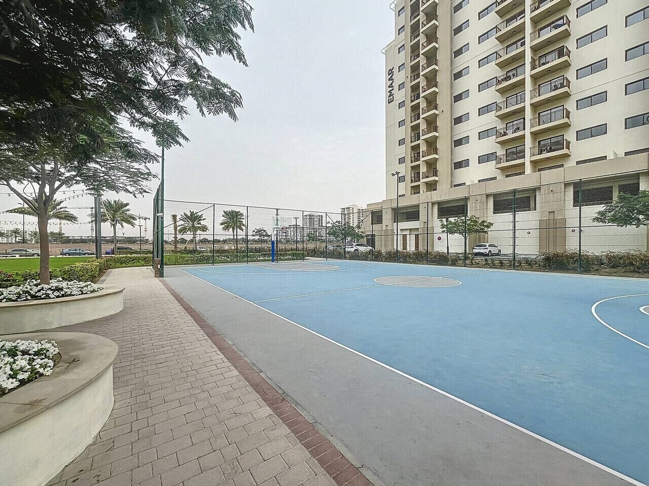 Ein Basketballplatz, umzäunt, mit einem hohen Gebäude im Hintergrund.