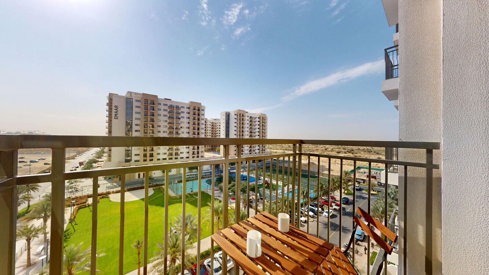 Een balkon met uitzicht op een zwembad, omliggende gebouwen en een groen gazon.