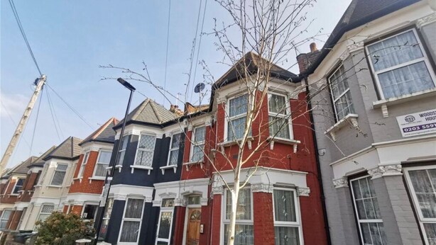 Una hilera de casas adosadas de diferentes estilos arquitectónicos, incluyendo una casa de ladrillo rojo con detalles blancos y una casa gris con un cartel de una empresa de administración de propiedades.