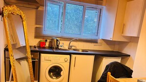 Una cocina compacta con lavadora, un lavamanos y una ventana con persianas.