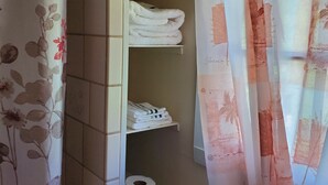 A bathroom with a tiled wall, a shelf with folded towels, a toilet paper roll, and a shower curtain with floral patterns. - Charming 1-bedroom apt Buffalo WY, on creek, AC,  WiFi, & 1 block from downtown. (Buffalo)