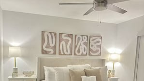 Une chambre à coucher comprenant un lit, deux tables de chevet, un ventilateur de plafond et des œuvres d’art murales.