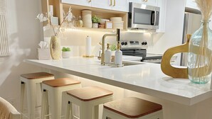 Une cuisine moderne avec des meubles blancs, un four à micro-ondes en acier inoxydable et un îlot central doté de tabourets de bar.