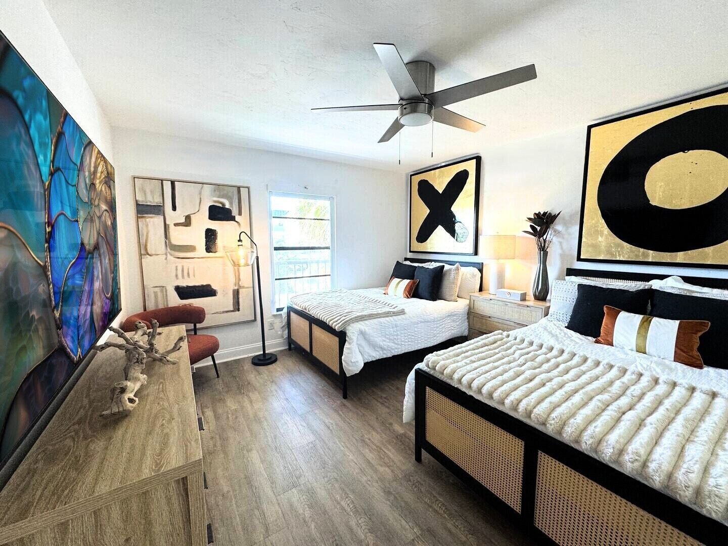 Una camera da letto moderna con due letti, una ventola a soffitto e opere d'arte astratte alle pareti.