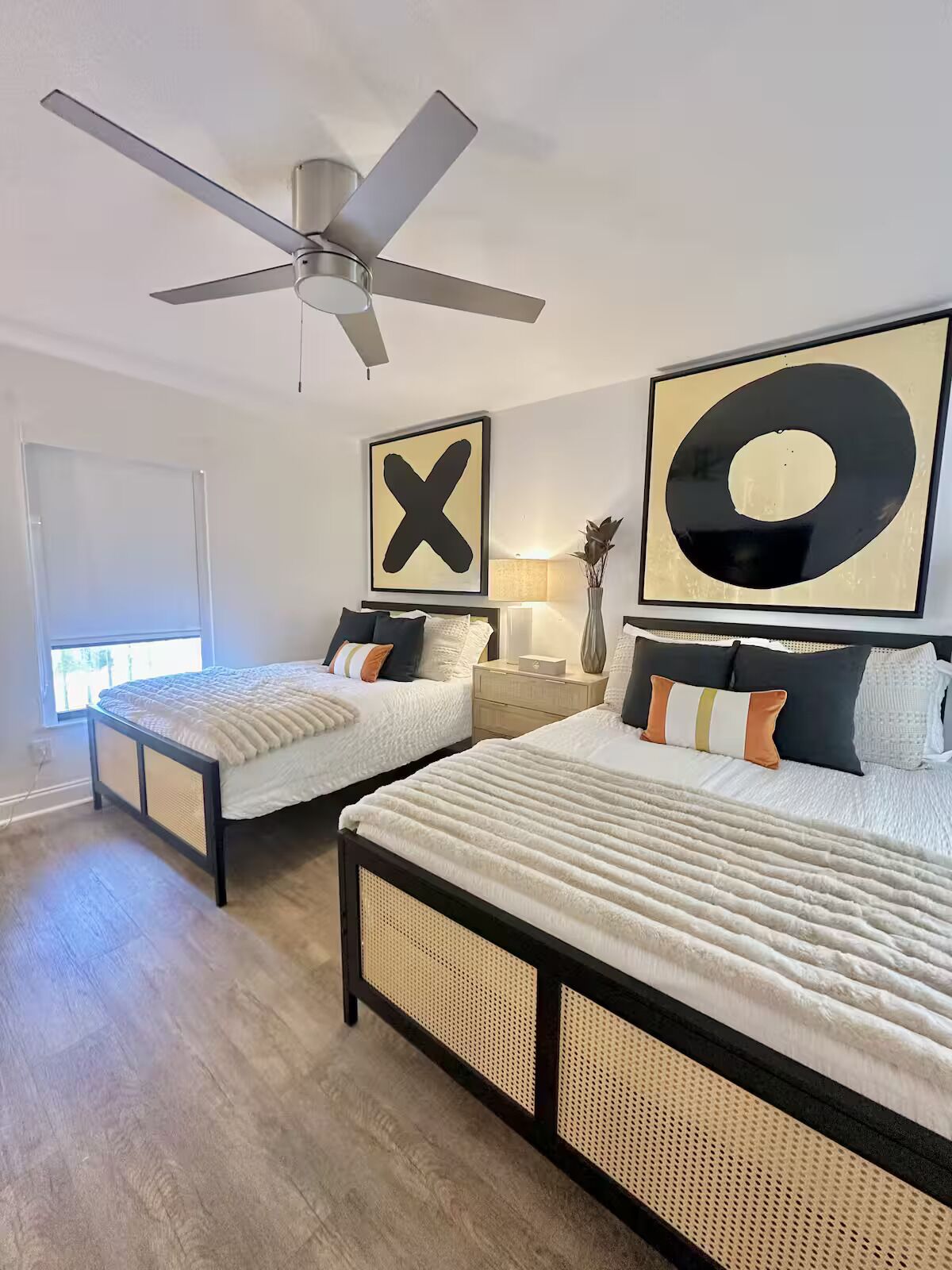 A bedroom with two beds, a ceiling fan, and large wall art.