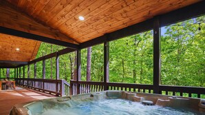 A hot tub area with a wooden deck and a view of a forest.