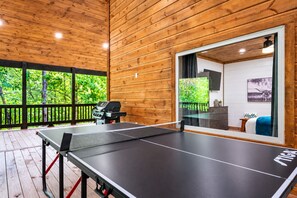 Una mesa de ping pong en una sala de madera con vistas a zonas verdes.