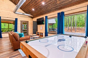 Un interior de madera con una mesa de billar, un sofá y vistas al exterior.