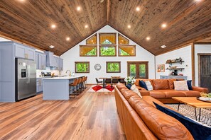 A spacious kitchen with a central island, wooden ceiling, and large windows.