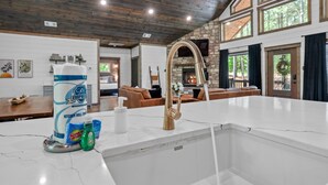 A modern kitchen with a white marble countertop, a gold faucet, and a stone backsplash. There is a large bottle of detergent and a soap dispenser on the counter.