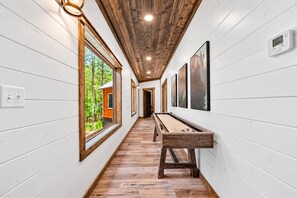 A hallway with wooden floors, white walls, and a wooden ceiling. There is a pool table in the center, and a thermostat on the wall. - Creekside Cabin | Hot Tub | Games & Fire Pit (Broken Bow)