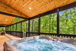 Een hottubgedeelte met een houten terras en grote ramen met uitzicht op een bos.