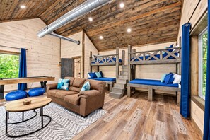 Interior acogedor de una cabaña con techo de madera, un sofá, una mesa y una litera.