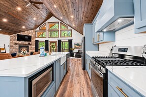 Una cocina moderna con una isla central, una chimenea de piedra y un amplio ventanal con vistas a un bosque.