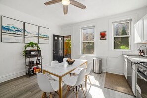 A modern kitchen with white cabinetry, a dining table with chairs, a ceiling fan, and artwork on the walls. - Near UPMC, CMU, Pitt & Walnut + Free Parking (Pittsburgh)