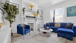 Una sala de estar con un sofá azul, un sillón azul, una chimenea blanca y un ventanal grande.