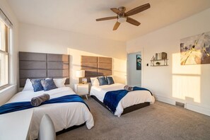 A hotel room with two beds, a ceiling fan, a nightstand, a lamp, a painting, and a bookshelf. - Near UPMC, CMU, Pitt & Walnut + Free Parking (Pittsburgh)
