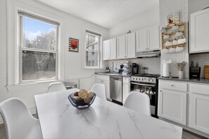 A modern kitchen with white cabinets, a marble countertop, and a dining area with a white table and chairs. - Near UPMC, CMU, Pitt & Walnut + Free Parking (Pittsburgh)