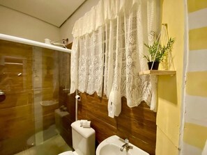 A bathroom with a glass shower enclosure, a toilet, a sink, and a decorative lace curtain. - Kambô Guest House (Sao Paulo)