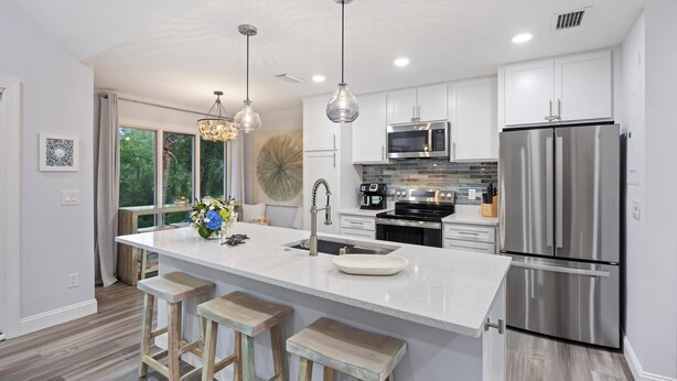 Una cocina moderna con armarios blancos, electrodomésticos de acero inoxidable y una isla grande con taburetes.