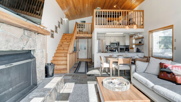 Un grand salon doté d’une cheminée, d’une table à manger et d’un canapé. Un escalier mène à un niveau supérieur où se trouve un balcon.