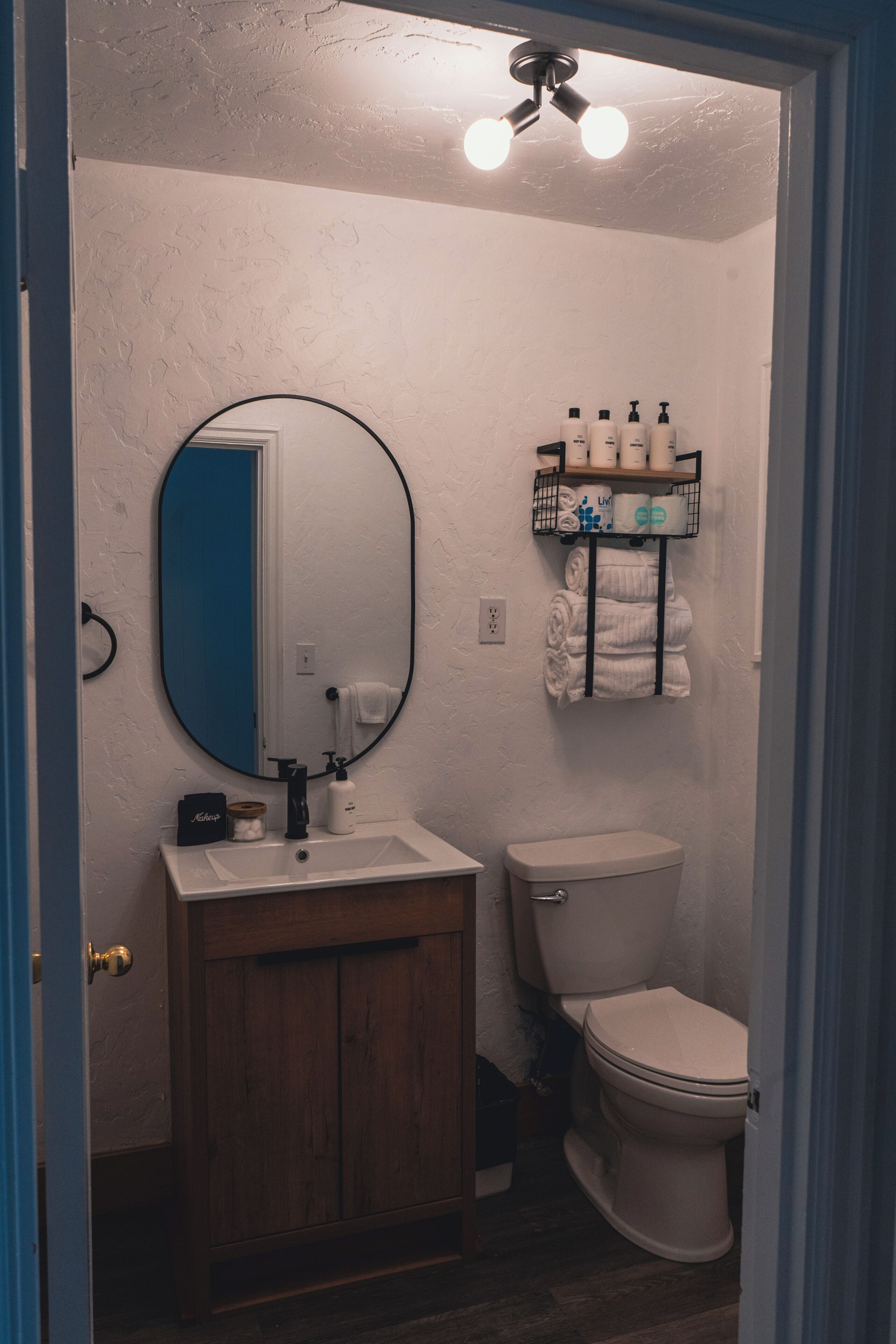 Un baño con lavamanos blanco, un espejo, un inodoro y una repisa con artículos de aseo.