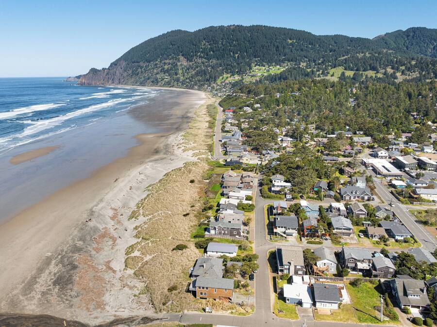 Zona residencial costera con casas a lo largo de la playa y un paisaje montañoso de fondo.