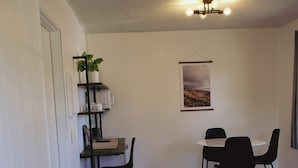 A living room with a gray sofa, a dining area with a table and chairs, and a small bookshelf with a plant. - The Spinn (Manzanita)