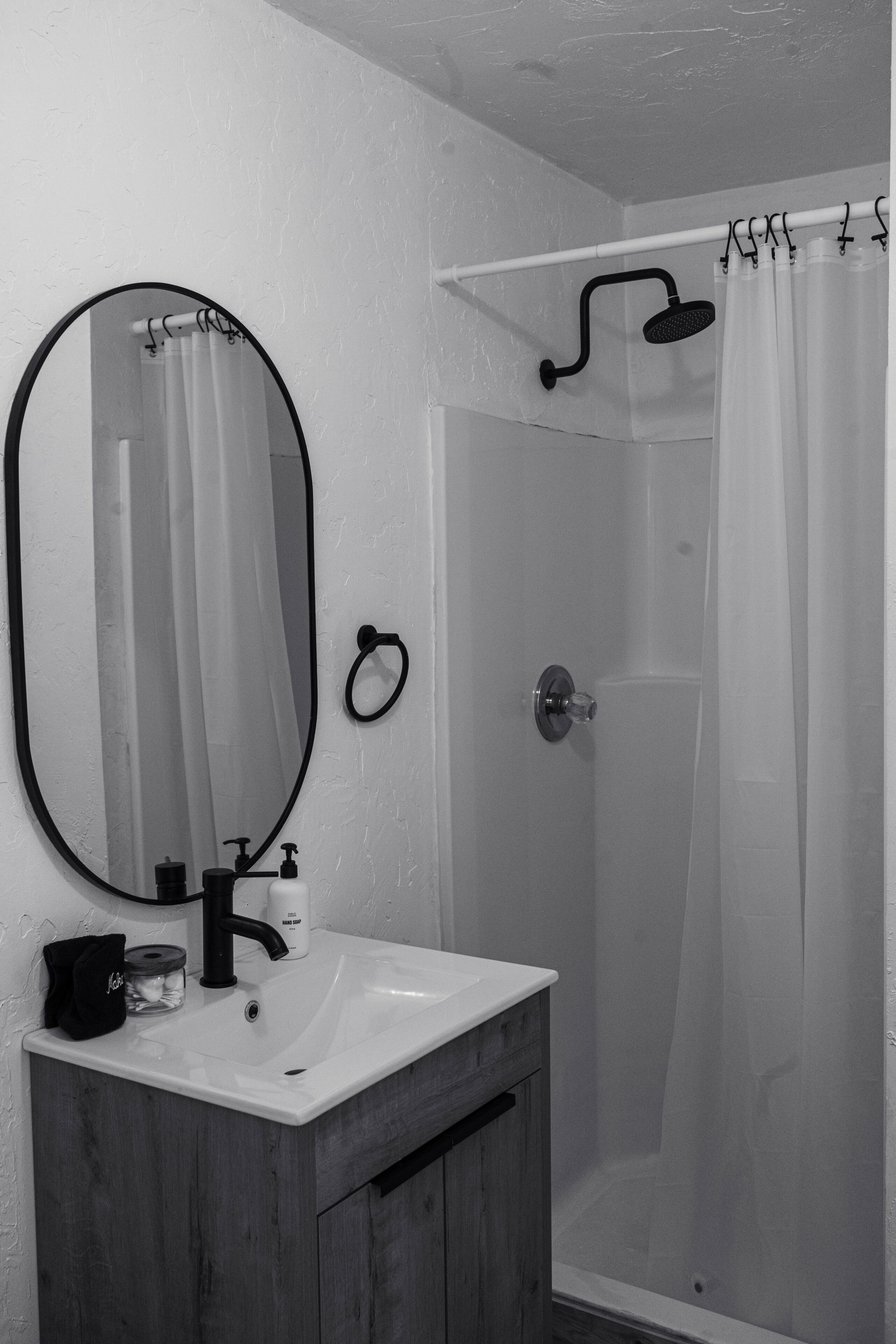 Ein Badezimmer mit weißem Waschbecken, einem Spiegel, einer Duschkabine mit Vorhang und einem Handtuchhalter.