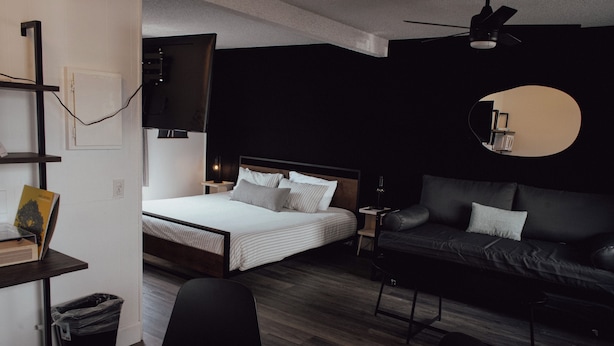 A modern hotel room with a bed, a sofa, a desk with a chair, and a TV mounted on the wall. - The Spinn (Manzanita)
