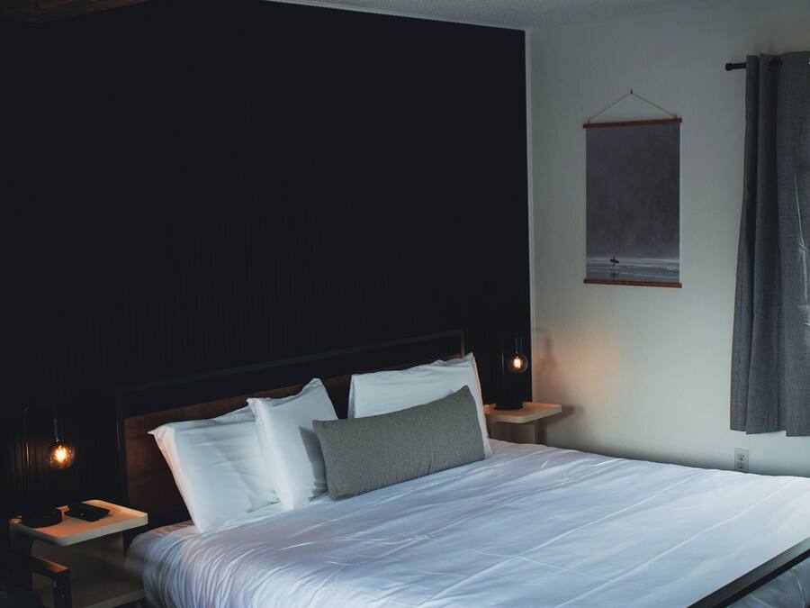 Een slaapkamer met een groot bed, twee nachtkastjes, een hanglamp en een raam met gordijnen.