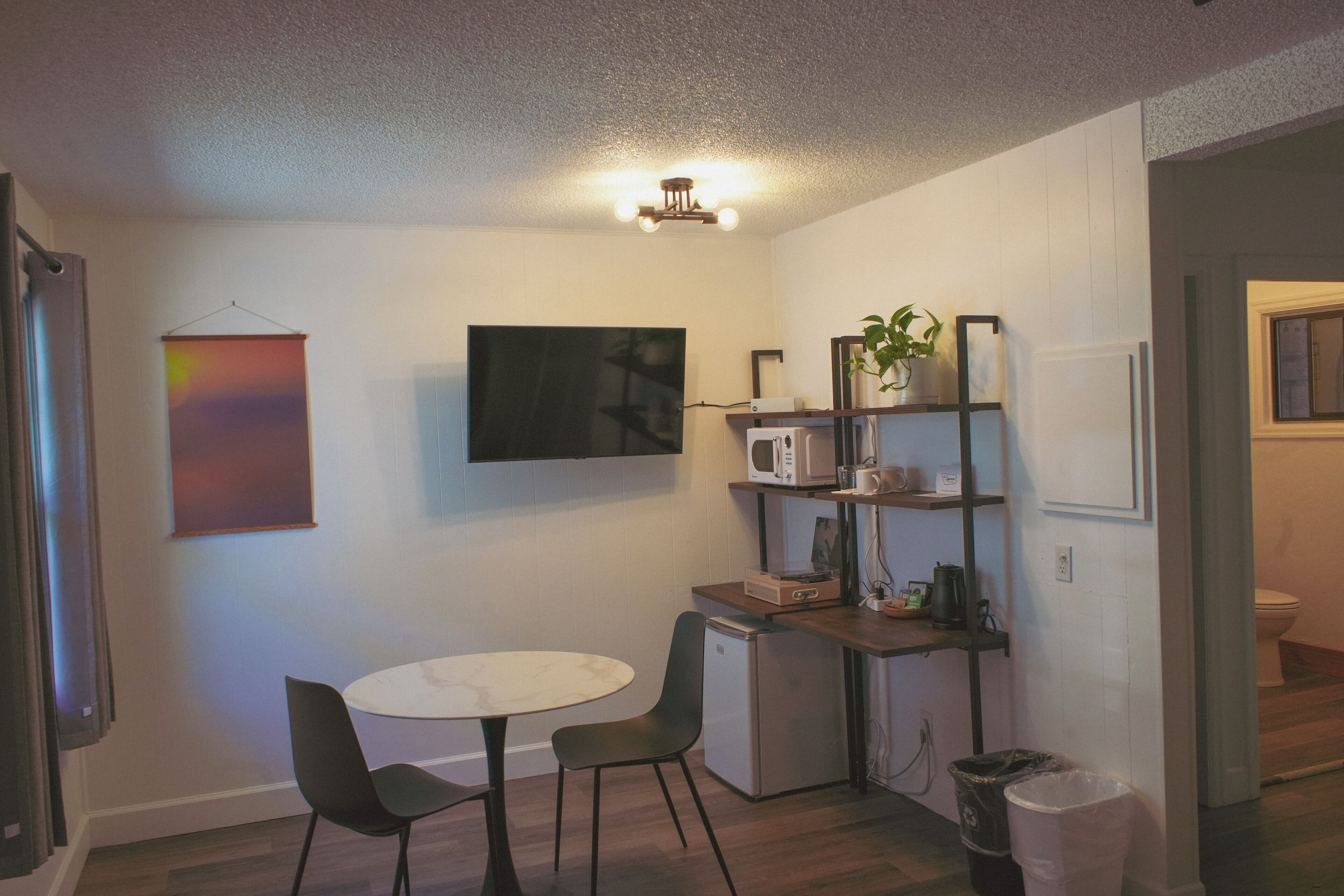 Cocina compacta con microondas, refrigerador pequeño y comedor con dos sillas y una mesa.