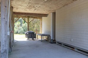 A covered outdoor area with a table and a grill, wooden beams, and a concrete floor. - Joint Venture: Private Pool, Short Walk to Beach and Currituck Lighthouse (Corolla)
