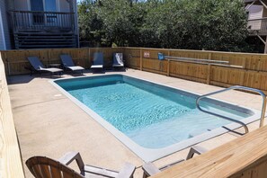 Piscina rectangular con muelle de madera alrededor, equipada con sillones de descanso y una escalera para la piscina.