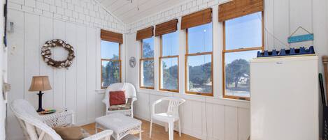 A room with white wicker furniture, a ceiling fan, and large windows with wooden blinds.