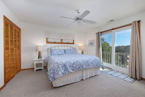 A bedroom with a bed, a nightstand, a ceiling fan, a window with curtains, and a view of the outdoors. - Joint Venture: Private Pool, Short Walk to Beach and Currituck Lighthouse (Corolla)