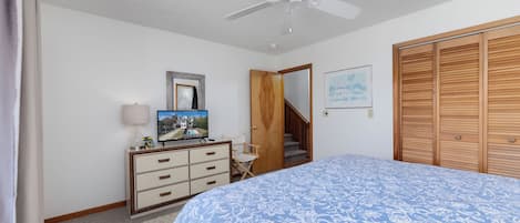 A bedroom with a bed, a dresser, a ceiling fan, a framed picture, a wooden door, and a staircase.