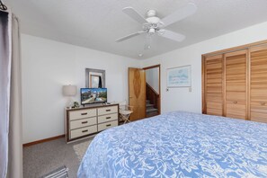 A bedroom with a bed, a dresser, a ceiling fan, a framed picture, a wooden door, and a staircase. - Joint Venture: Private Pool, Short Walk to Beach and Currituck Lighthouse (Corolla)