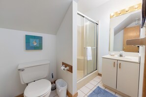 Un baño con inodoro, ducha, lavamanos y espejo.
