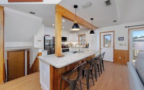 A spacious kitchen with a central island, bar stools, and a large window providing a view of the outdoors. - Joint Venture: Private Pool, Short Walk to Beach and Currituck Lighthouse (Corolla)